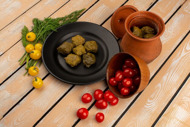 Draufsicht Dolma berühmtes östliches Hackfleisch innerhalb der schwarzen Platte zusammen mit roten Tomaten und Gelb auf dem Holzboden