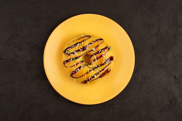 Draufsicht Donuts mit bunten Bonbons und Schokolade in orange Platte auf dem dunklen Boden