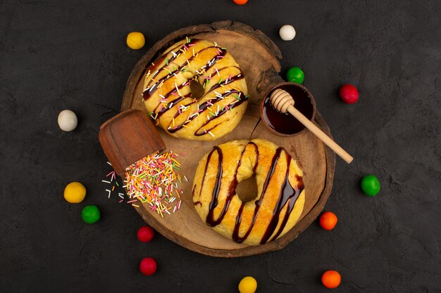 Draufsicht Donuts süß lecker lecker mit Schoko-Linien und bunten Süßigkeiten auf dem braunen Schreibtisch und dem dunklen Boden