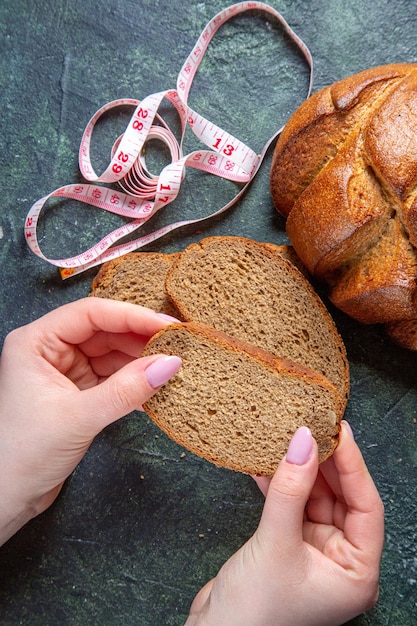 Draufsicht dunkle brotlaibe mit weiblichen händen auf dunklem schreibtisch