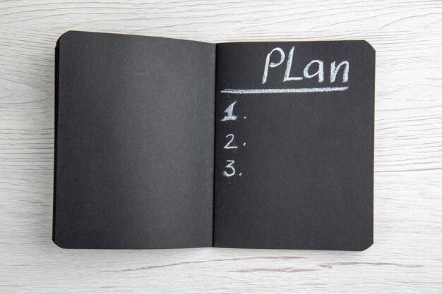 Draufsicht dunkler Notizblock mit plangeschriebener Liste auf weißem Hintergrund, der Büroarbeitszeitplanregime-Job-Schreibbuchgeschäft zeichnet