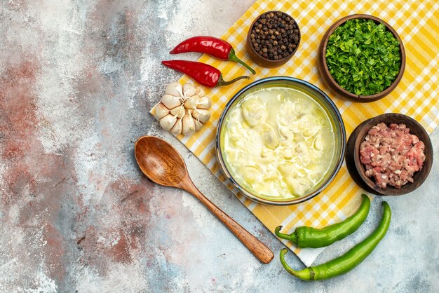 Draufsicht Dushbara Knödelsuppe in einer Schüssel Knoblauch Peperoni Holzlöffel Schalen mit Fleisch Pfeffer und Gemüse auf nackter Oberfläche mit Kopierraum