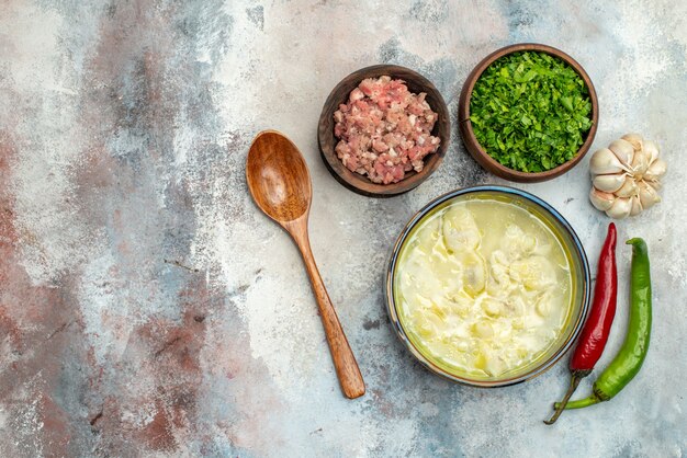 Draufsicht Dushbara Knödelsuppe in einer Schüssel Knoblauch Peperoni Holzlöffel Schalen mit Fleisch und Gemüse auf nackter Oberfläche mit Kopierraum