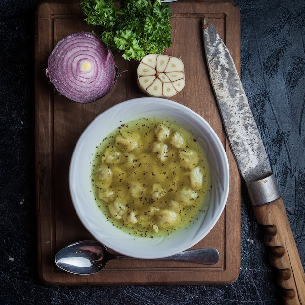 Draufsicht Dushpara mit Messer und Löffel und Zwiebel und Knoblauch im Lebensmittelbrett