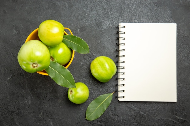 Kostenloses Foto draufsicht eimer mit grünen tomaten und lorbeer hinterlässt ein notizbuch und tomaten auf dunklem hintergrund