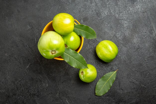 Draufsicht Eimer mit grünen Tomaten und Lorbeerblättern und Tomaten auf dunklem Hintergrund