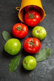 Draufsicht eimer mit roten und grünen tomaten und lorbeerblättern auf dunklem hintergrund
