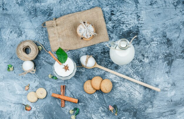 Draufsicht ein Krug Milch und eine Glasschale Joghurt mit Löffeln, Keksen, Eiern, Clew, Zimt und einer Pflanze auf dunkelblauer Marmoroberfläche. horizontal