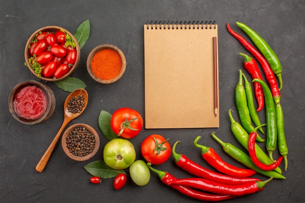 Draufsicht eine Schüssel Kirschtomaten scharfe rote und grüne Paprikaschoten und Tomaten Lorbeerblätter Schalen mit Ketchup-Paprika-Pulver und schwarzem Pfeffer und ein Notizbuch auf dem Boden