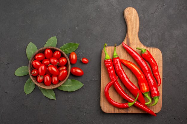 Draufsicht eine Schüssel Kirschtomaten und Lorbeerblätter und scharfe rote Paprikaschoten auf dem Schneidebrett in der Mitte des schwarzen Tisches