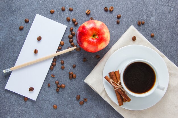 Draufsicht eine Tasse Kaffee mit Apfel, trockenem Zimt, Bleistift und Notizbuch auf grauer Oberfläche. horizontal