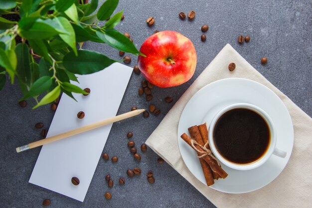 Draufsicht eine Tasse Kaffee mit Apfel, trockenem Zimt, Pflanze, Bleistift und Papier auf grauer Oberfläche. horizontal
