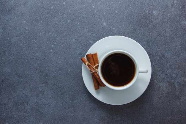 Draufsicht eine Tasse Kaffee mit trockenem Zimt auf grauer Oberfläche. horizontaler Raum für Text