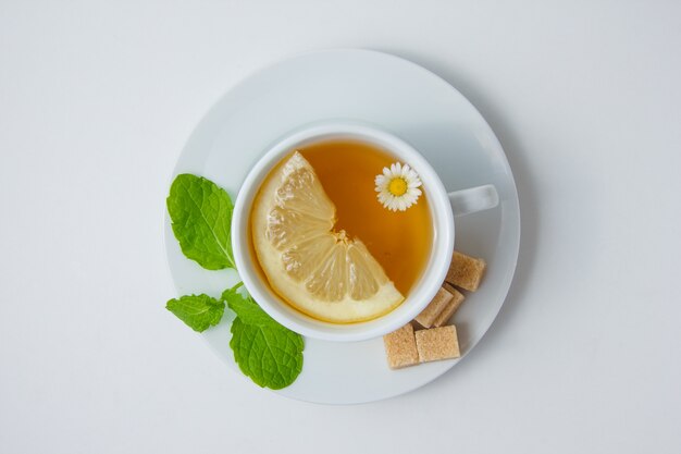 Draufsicht eine Tasse Kamillentee mit Zitrone, Minzblättern, Zucker auf weißer Oberfläche. horizontal