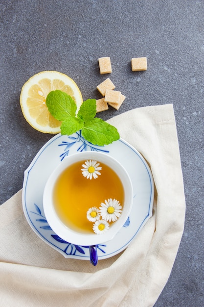 Draufsicht eine Tasse Kamillentee mit Zucker, Blättern, Zitrone auf Stoff