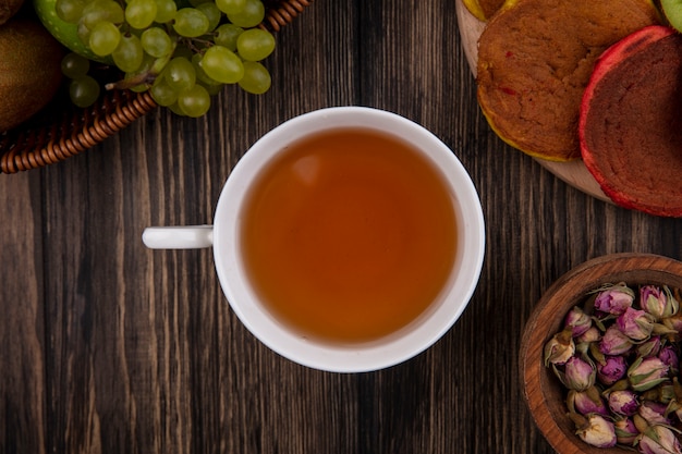 Draufsicht eine tasse tee mit bunten pfannkuchen auf einem ständer und mit grünen trauben auf einem hölzernen hintergrund