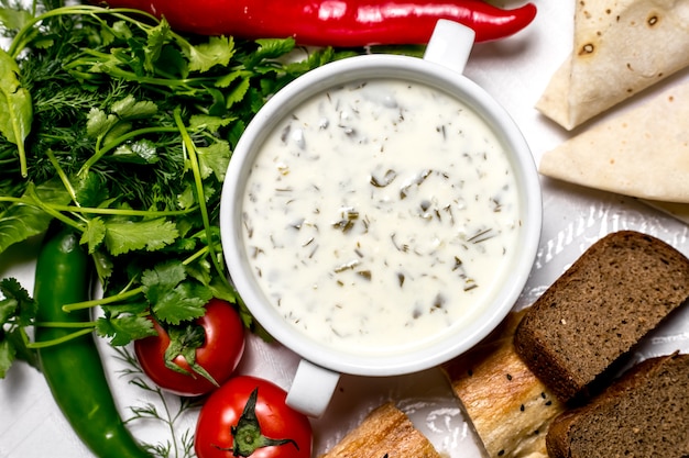 Draufsicht eine traditionelle aserbaidschanische Gericht-Dovga-Joghurtsuppe mit Kräutertomaten und Brot