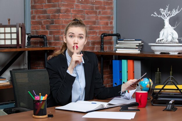 Draufsicht einer besorgten Frau, die an einem Tisch sitzt und ein Dokument hält, das im Büro eine Stillegeste macht