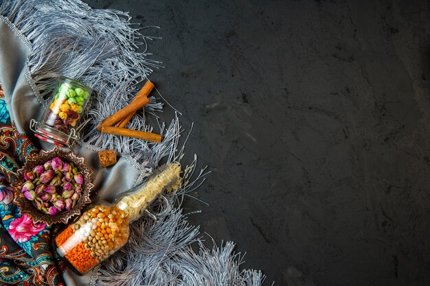 Draufsicht einer Flasche mit rohen Maissamen und Bohnen getrockneten Rosenknospen und Zimtstange auf einem Schal mit Quaste mit Kopienraum auf Schwarz