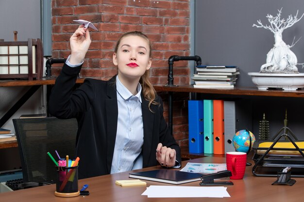 Draufsicht einer jungen Büroangestellten, die an ihrem Schreibtisch sitzt und Papierflieger spielt