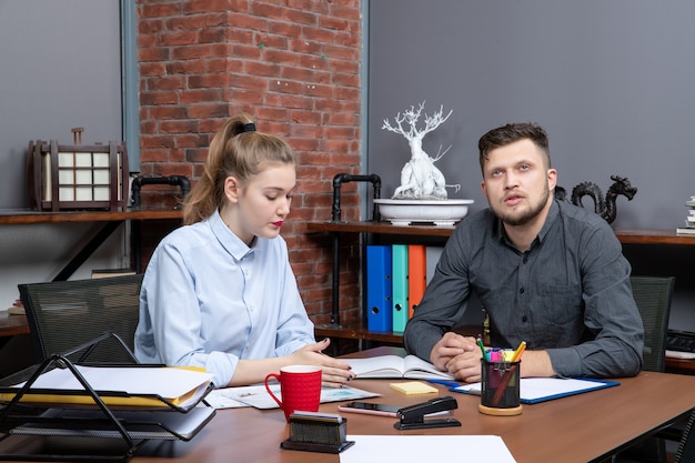 Draufsicht einer jungen Büroassistentin und ihres männlichen Kollegen, die am Tisch sitzen und ein wichtiges Thema im Büro diskutieren