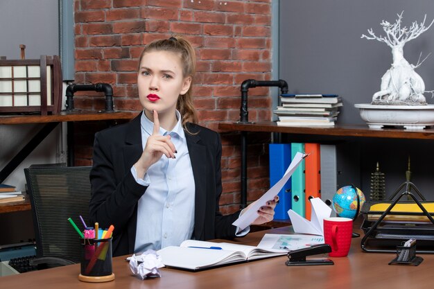Draufsicht einer jungen Dame, die an einem Tisch sitzt und das Dokument im Büro nach oben zeigt