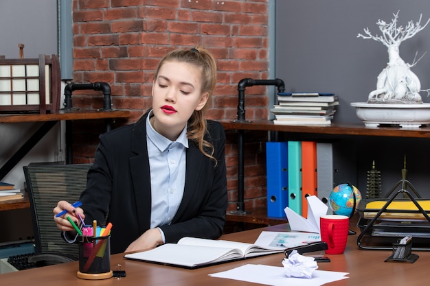 Draufsicht einer jungen Dame, die an einem Tisch sitzt und im Büro einen Stift im Federmäppchen arrangiert