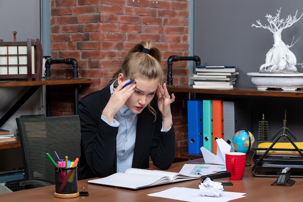 Kostenloses Foto draufsicht einer jungen dame, die an einem tisch sitzt und sich im büro sorgfältig auf etwas konzentriert