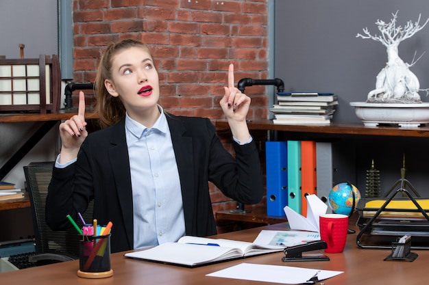 Draufsicht einer jungen Frau, die an einem Tisch sitzt und im Büro nach oben zeigt