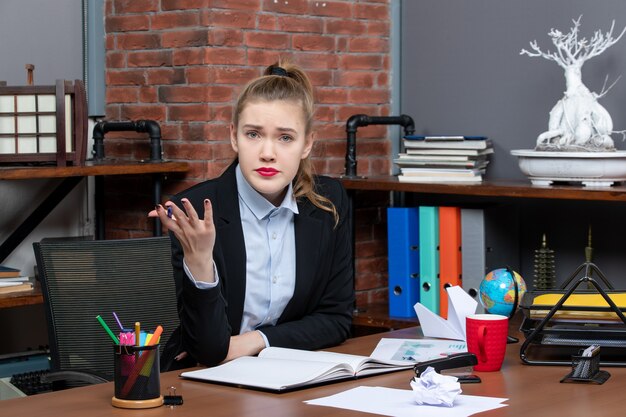 Draufsicht einer jungen Frau, die an einem Tisch sitzt und jemanden im Büro befragt in