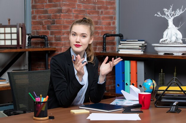 Draufsicht einer jungen neugierigen Büroangestellten, die an ihrem Schreibtisch sitzt und für die Kamera posiert