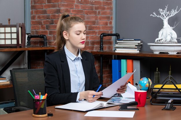 Draufsicht einer jungen selbstbewussten Assistentin, die an einem Tisch sitzt und ein Dokument im Büro liest reading