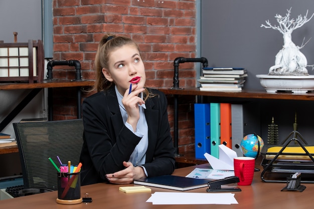 Draufsicht einer jungen, unsicheren, unsicheren Büroangestellten, die an ihrem Schreibtisch sitzt und für die Kamera posiert
