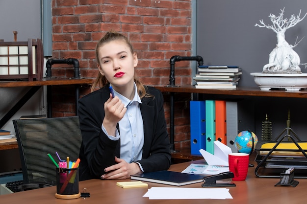 Kostenloses Foto draufsicht einer jungen verwirrten assistentin, die an ihrem schreibtisch im büro sitzt sitting