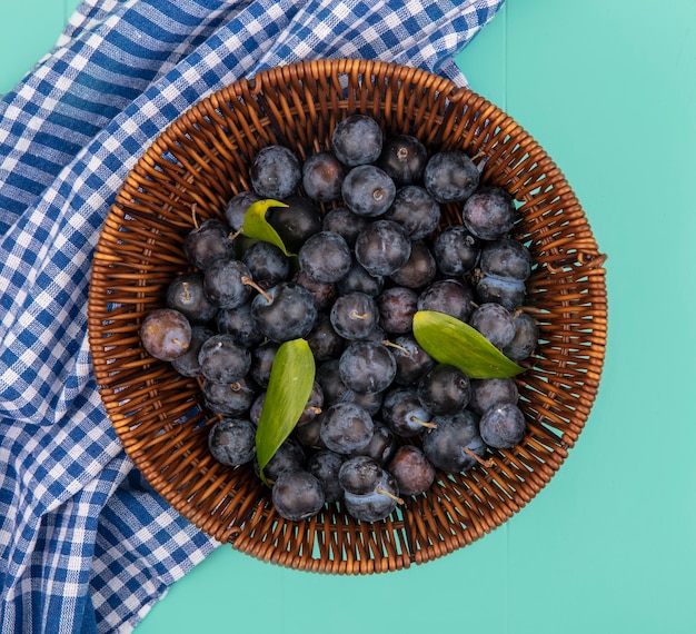 Draufsicht einer kleinen sauren Frucht mit einer dunklen Hautschleier auf einem Eimer auf einer blau karierten Tischdecke auf einem blauen Hintergrund