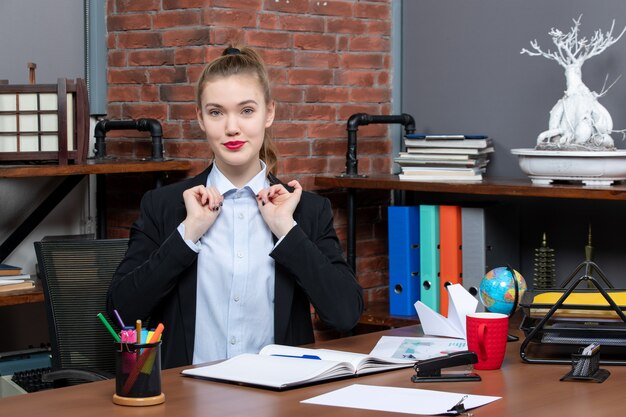 Draufsicht einer lächelnden jungen Frau, die an einem Tisch sitzt und sich auf etwas im Büro konzentriert