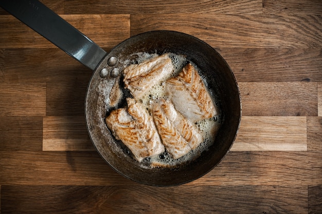 Draufsicht einer Pfanne mit gebratenem Fleisch auf einem Holztisch