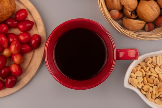 Draufsicht einer roten Tasse Kaffee mit Kornelkirschen auf einem hölzernen Küchenbrett mit Nüssen auf einem Eimer auf einer grauen Wand