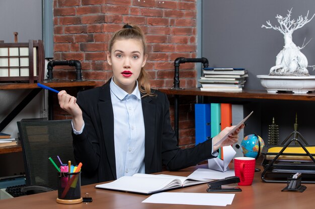 Draufsicht einer schockierten jungen Frau, die an einem Tisch sitzt und ein Dokument im Büro hält in