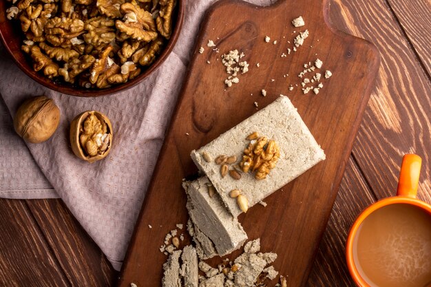 Draufsicht einer Schüssel mit Walnüssen und süßen Halva-Scheiben auf einem Holzbrett