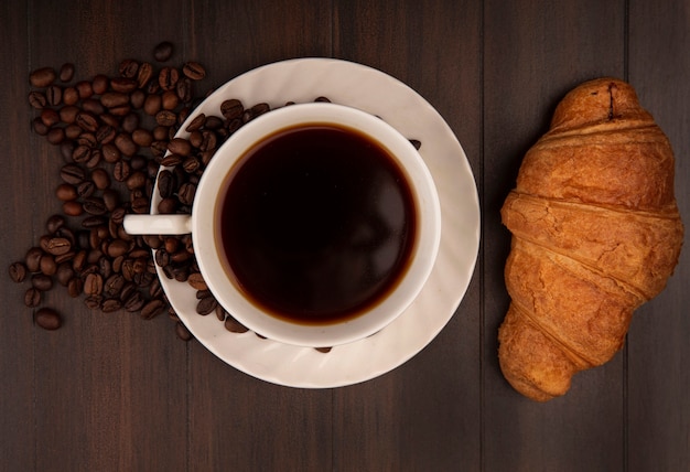 Draufsicht einer Tasse Kaffee mit Croissant mit Kaffeebohnen lokalisiert auf einer Holzwand