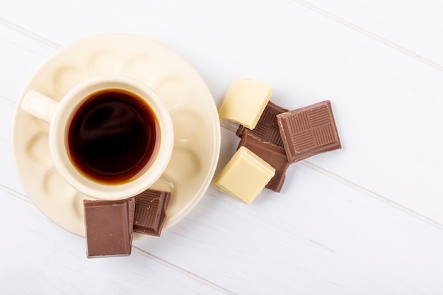 Draufsicht einer Tasse Kaffee mit weißer und dunkler Schokolade auf weißem hölzernem Hintergrund