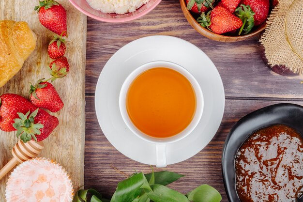 Draufsicht einer Tasse Tee mit frischer reifer Erdbeermarmelade und Hüttenkäse auf rustikalem Holz