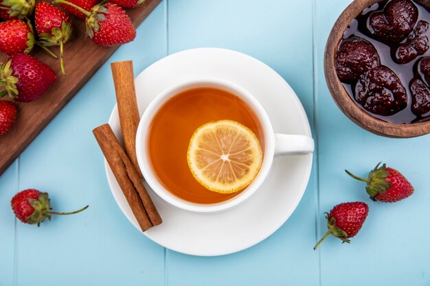 Draufsicht einer Tasse Tee mit Zimtstangen mit Erdbeermarmelade auf einer Holzschale auf einem blauen Hintergrund