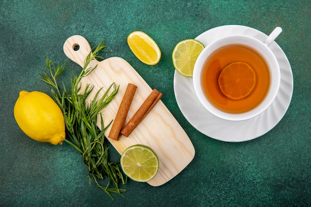Draufsicht einer Tasse Tee mit Zitronen und Zimtstangen auf hölzernem Küchenbrett auf gre