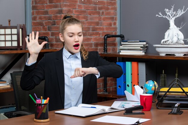 Draufsicht einer überraschten jungen Frau, die an einem Tisch sitzt und ihre Zeit im Büro überprüft