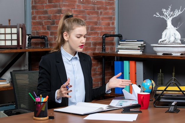 Draufsicht einer verwunderten jungen frau, die an einem tisch sitzt und sich auf etwas im büro konzentriert