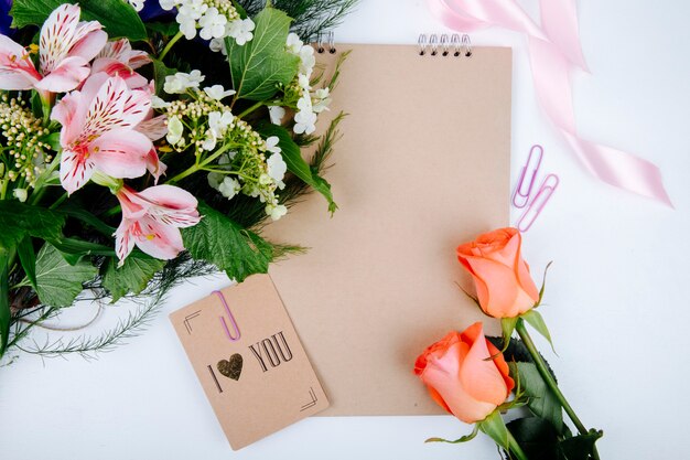 Draufsicht eines Blumenstraußes der rosa Farbe Alstroemeria Blumen mit blühendem Viburnum und einem Skizzenbuch mit einer Postkarte und Korallenfarbe Rosen auf weißem Hintergrund