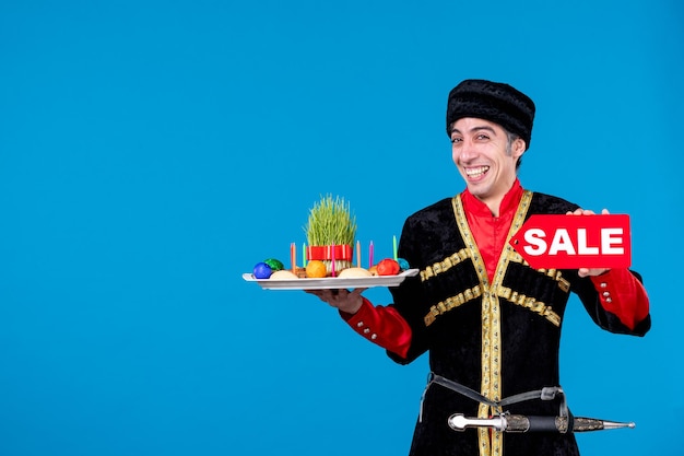 Kostenloses Foto draufsicht eines glücklichen jungen erwachsenen in traditioneller kleidung, der ein tablett mit nationalen süßwaren gibt und das verkaufssymbol auf blauem wellenhintergrund zeigt