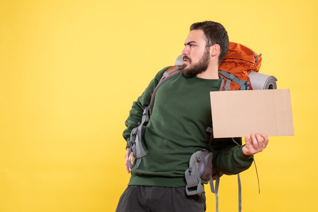 Draufsicht eines jungen wütenden reisenden Kerls mit Rucksack, der ein Blatt hält, ohne auf Gelb zu schreiben